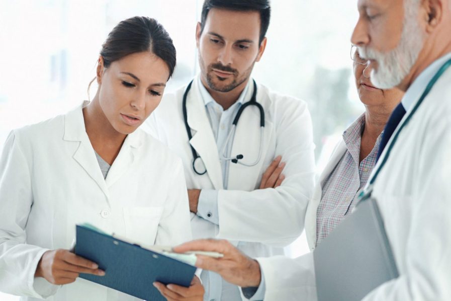 Closeup front view of small group of mixed age doctors having a hallway meeting. There are two senior doctors, 30's intern and a nurse. Senior male doctor is giving some tips and directions.